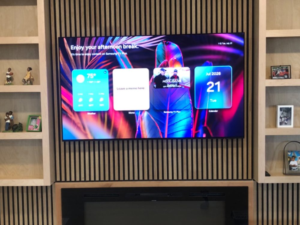 TV mounted on a slat wall between built-in shelves, above a linear fireplace
